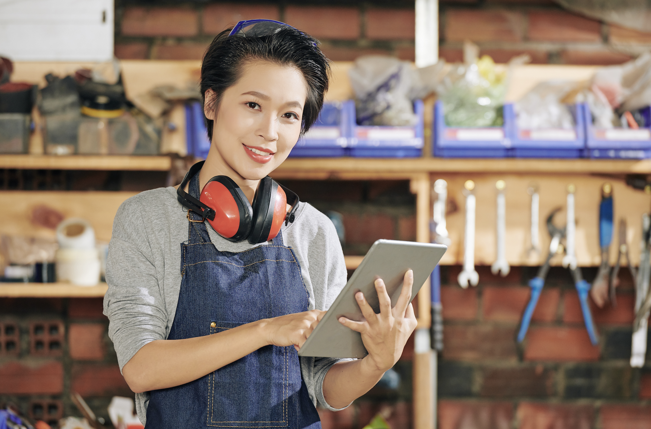 a smiling woman in overalls and headphones smiling with a tablet