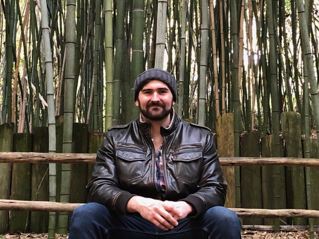 a smiling man posing in front of bamboo