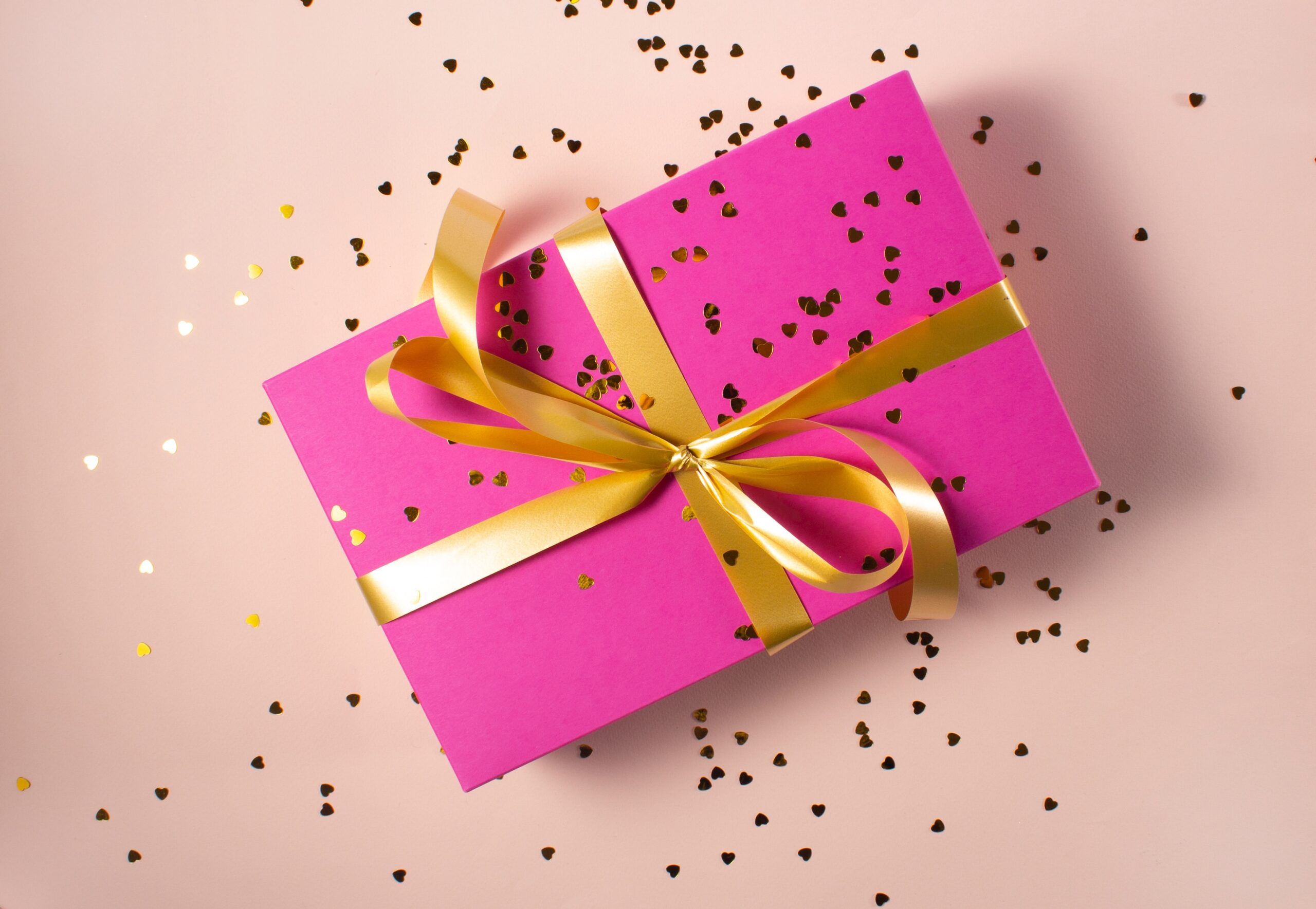 a pink and gold wrapped present with glitter hearts surrounding it