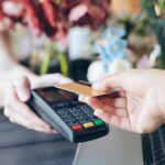 Close-up of seller holding terminal for contactless payment in flower store, customer putting credit card to terminal.